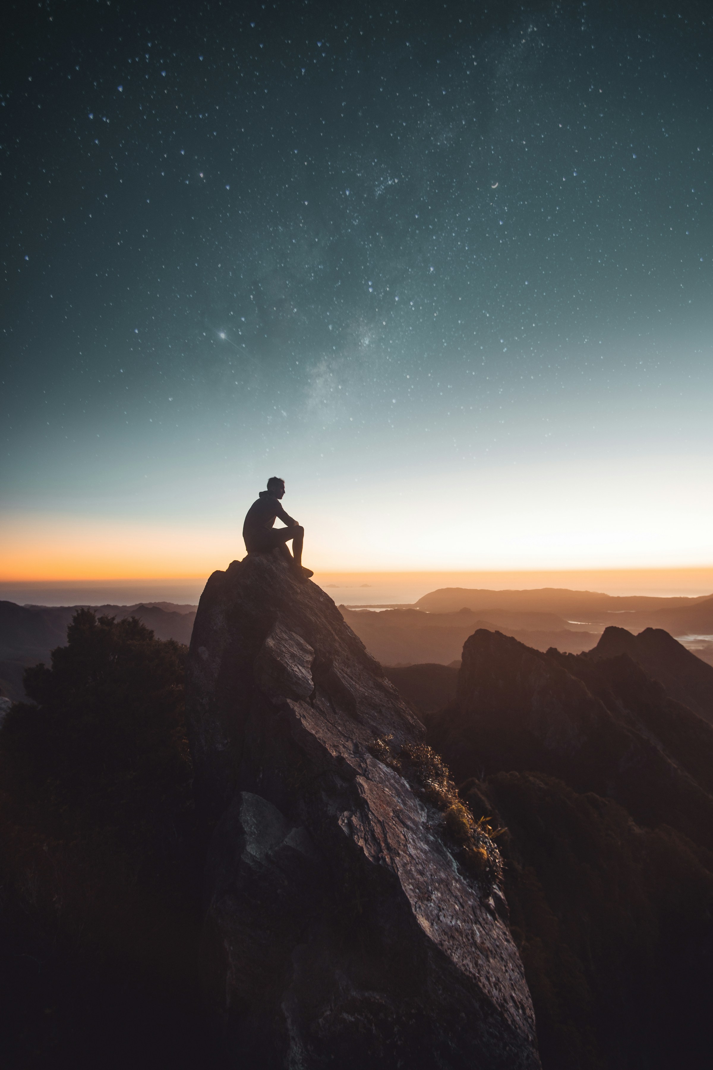 Person sitting on a mountain ridge looking towards the horizon